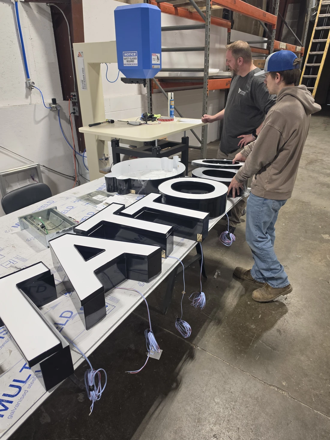 Two team members working beside fabricated channel letters on a shop worktable