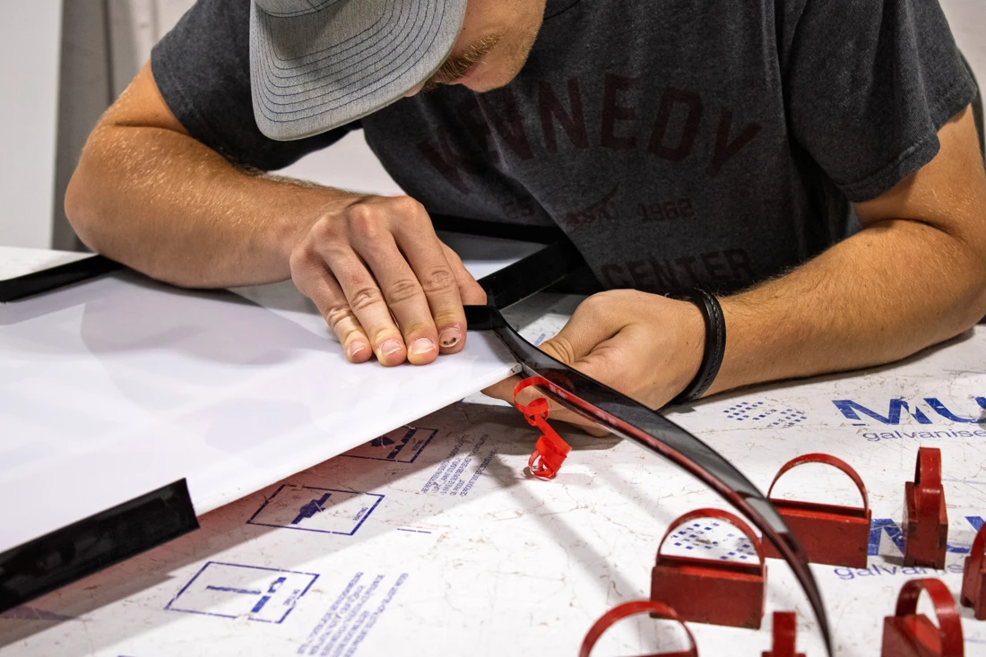 Hands fitting black trim around a white channel-letter face in our fabrication shop